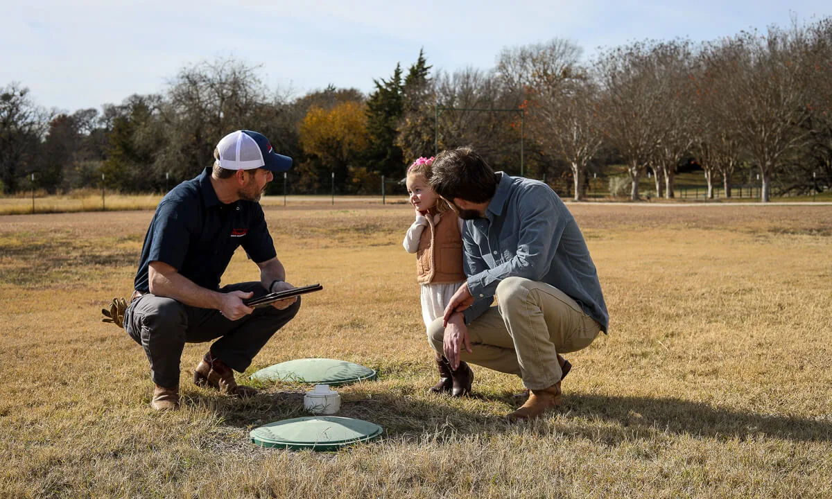 HomeField technician kneeling at a septic lid with a homeowner