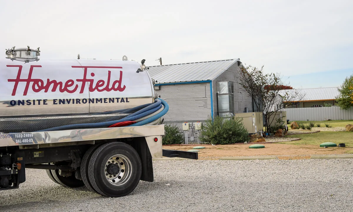 HomeField pump truck parked beside septic risers at a commercial property