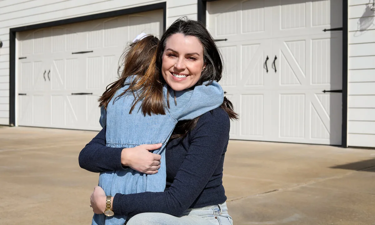 Mother hugging her daughter in front of their home