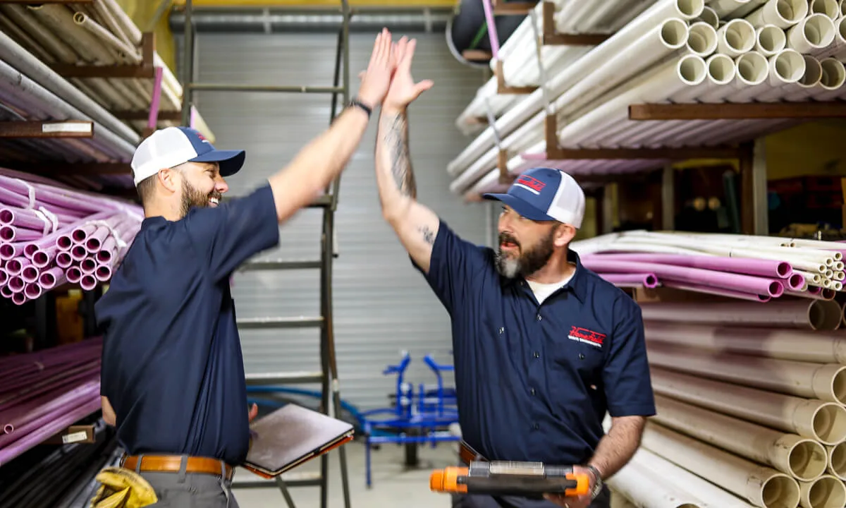 Two HomeField crew members celebrating a finished job among pipe and fittings
