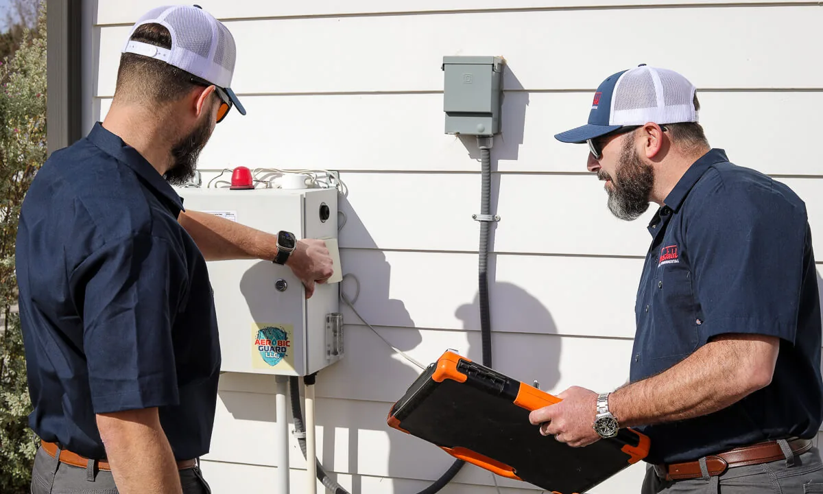 Two HomeField technicians checking an aerobic septic control panel