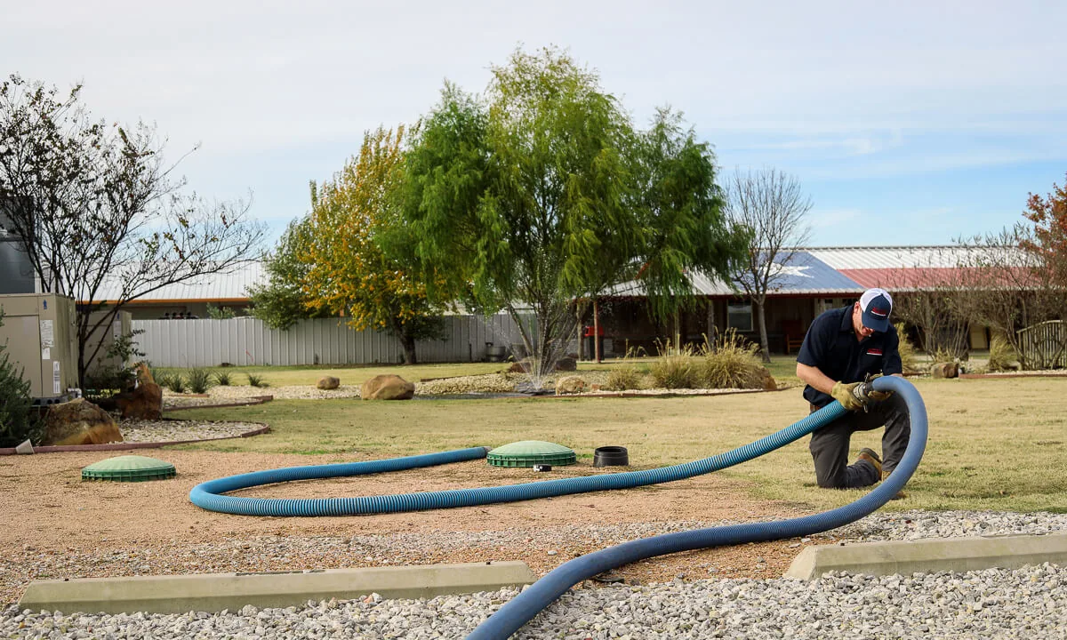 HomeField technician coiling a hose beside an open commercial septic system