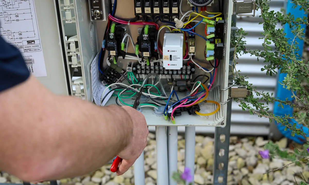 Gloved hand checking wiring inside an open septic control panel
