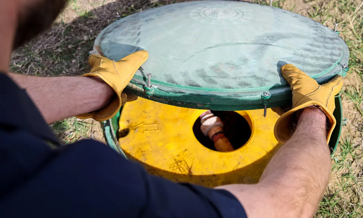 Gloved HomeField technician lifting a septic lid to show the inner lid