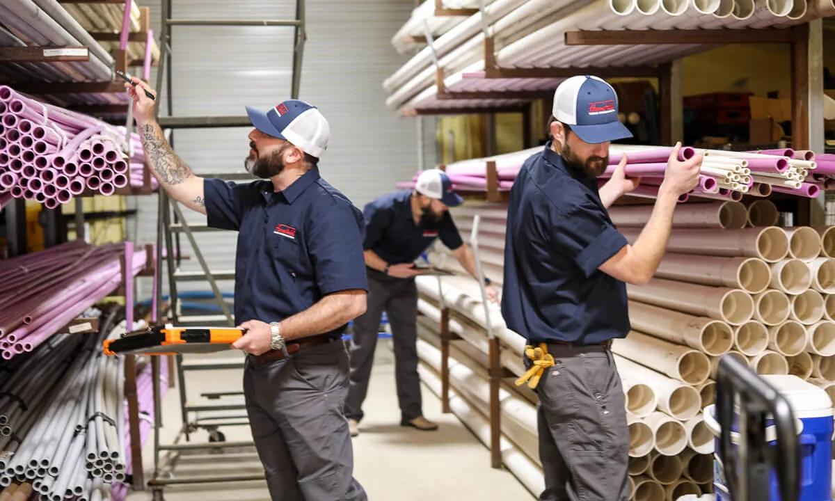 Three HomeField technicians getting pipe and supplies ready in a warehouse